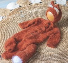 Load image into Gallery viewer, Knitted burnt orange baby outfit with white accents on a textured surface. Knitted fox-inspired footless romper with tail and matching fox bonnet presented on wooden ball.